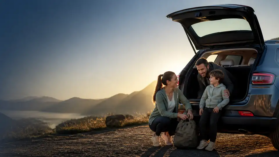 Imagem ilustrativa de uma família ao lado de um carro, diante de montanhas ao pôr do sol.